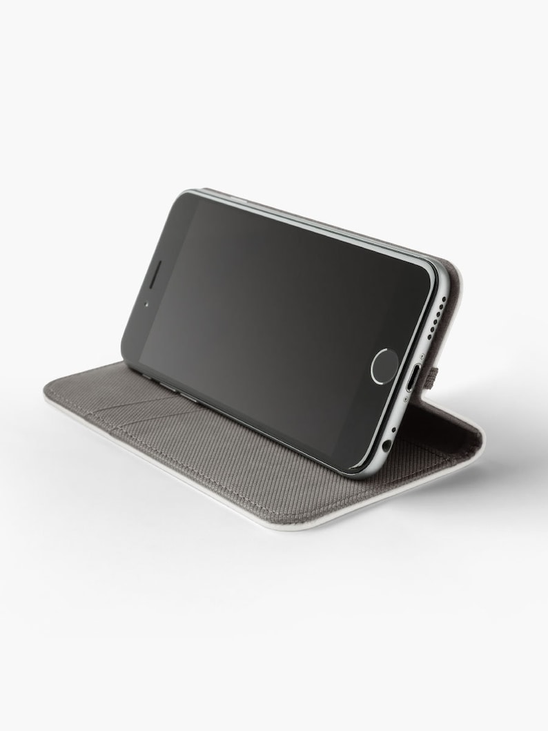 May include: A grey phone case with a black smartphone inside. The case is folded to create a stand for the phone.