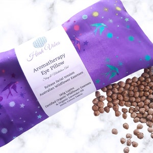 May include: Purple aromatherapy eye pillow with a floral print and the text "Hiah Vibes Aromatherapy Eye Pillow Step & Meditation Aid Release facial tension Australian Wildflower Essenses 180g Lupins Certified Organic Wildflower Essenses & Organic Lavender Oil 100% Cotton Fabric". The pillow is filled with brown lupin seeds.