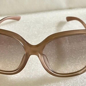K&ouml;nnte beinhalten: Braune Sonnenbrille mit einem abgerundeten, &uuml;bergro&szlig;en Rahmen. Die Gl&auml;ser haben eine Farbverlaufst&ouml;nung, die von einem dunkleren Farbton oben zu einem helleren Farbton unten &uuml;bergeht. Die B&uuml;gel sind farblich passend braun.