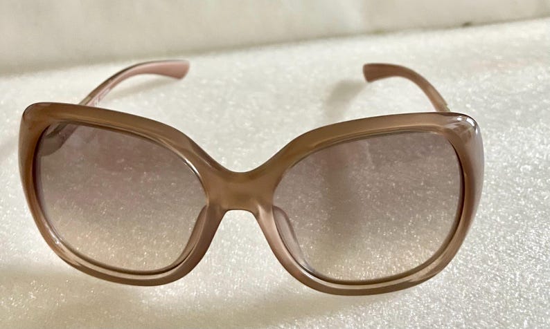 K&ouml;nnte beinhalten: Braune Sonnenbrille mit einem abgerundeten, &uuml;bergro&szlig;en Rahmen. Die Gl&auml;ser haben eine Farbverlaufst&ouml;nung, die von einem dunkleren Farbton oben zu einem helleren Farbton unten &uuml;bergeht. Die B&uuml;gel sind farblich passend braun.