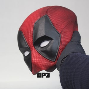 May include: Red and black Deadpool mask with a textured surface. The mask has a white eye shape and the text "DP3" is visible below the mask.