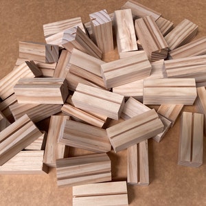 May include: A pile of natural wood display blocks with a groove cut into the top. The blocks are approximately 5 cm wide and 10 cm long.