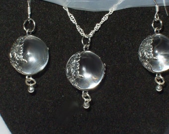 May include: A set of silver earrings and a necklace with clear crystal orbs. Each orb has a silver floral design.