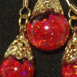 May include: A pair of red glass earrings with gold filigree accents. The earrings are teardrop shaped and have a sparkly, iridescent finish.