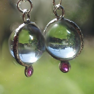 Puede incluir: Un par de pendientes de plata con esferas de cristal transparentes y pequeñas piedras preciosas rosas que cuelgan de la parte inferior.