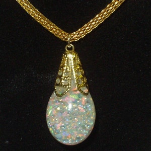 May include: A gold chain necklace with a teardrop-shaped pendant. The pendant is filled with iridescent glitter and has a gold filigree design.