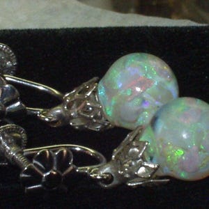 May include: A pair of silver clip-on earrings with iridescent opal stones. The stones are a light green and white colour with a hint of pink.