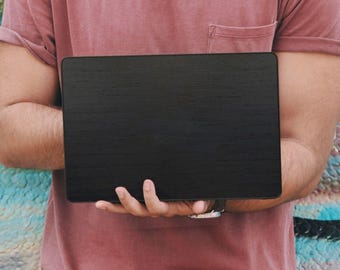 Puede incluir: Un portátil negro sostenido por una persona que lleva una camiseta rosa y gafas de sol. El fondo es una pared de graffiti colorida con pintura azul, verde y naranja.