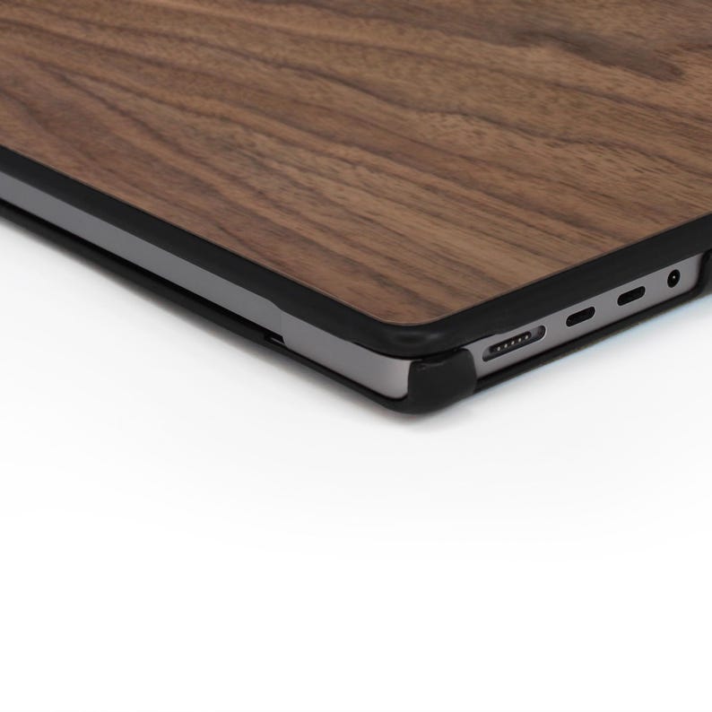 Puede incluir: Primer plano de un port&aacute;til con un acabado de veta de madera marr&oacute;n oscuro en la cubierta superior. El port&aacute;til tiene un borde negro y una base plateada. El dise&ntilde;o presenta una est&eacute;tica elegante y moderna.