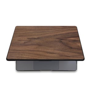 Puede incluir: Un ordenador port&aacute;til con una cubierta de madera. La cubierta tiene un patr&oacute;n de vetas de madera marr&oacute;n oscuro con un borde negro. El port&aacute;til es gris y tiene un dise&ntilde;o elegante y moderno. El patr&oacute;n de vetas de madera a&ntilde;ade un toque natural y elegante.