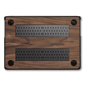 Puede incluir: Una funda de madera para port&aacute;til con un acabado de veta de madera marr&oacute;n oscuro. La funda tiene un marco negro y cuatro patas de goma negras. Se ven dos rejillas rectangulares con un dise&ntilde;o de malla plateada.