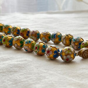 May include: A gold necklace with round beads decorated with colorful enamel floral patterns. The beads are connected with a silver clasp.