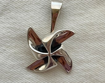 Könnte beinhalten: Ein silberner Windmühlen-Anhänger. Die Windmühle hat vier Flügel und eine Schlaufe oben zum Anbringen an einer Kette oder einem Armband.