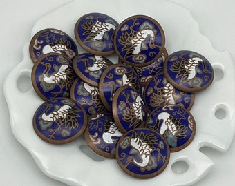 May include: A collection of 14 round, blue enamel buttons with white crane designs. The buttons have a copper-toned metal base.