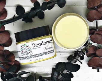 Puede incluir: Un tarro blanco con tapa negra y una etiqueta amarilla que dice "Desodorante Lavanda" y "Harmony Bath Goods". El tarro está lleno de un desodorante amarillo y está sobre una superficie blanca con hojas marrones.