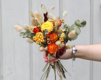 May include: A bouquet of dried flowers in shades of yellow, orange, and red. The bouquet includes dried grasses, eucalyptus, and other dried foliage.