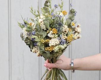 May include: A bouquet of dried flowers featuring muted green eucalyptus leaves, small clusters of yellow billy buttons, white yarrow, and sprigs of blue thistle. The stems are gathered together and tied with a thin piece of natural twine.