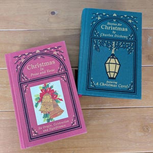 May include: Two vintage Christmas books. One is teal with gold lettering and a lantern illustration, titled "Stories for Christmas by Charles Dickens." The other is pink, titled "Christmas in Prose and Verse" with a bell illustration.