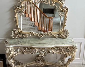 May include: A white and gold ornate console table with a green marble top and a matching ornate mirror. The mirror reflects a staircase with a wooden railing.