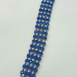 May include: A dazzling bracelet featuring rows of vibrant blue gemstones set in a silver-tone metal. The bracelet has a secure clasp closure. The gemstones are round and faceted, catching the light. A beautiful piece of jewelry.