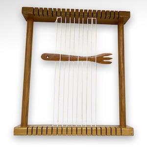 May include: A wooden loom with a wooden shuttle and white string. The loom is made of natural wood and has a simple design.
