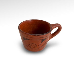 May include: A small, hand-crafted terracotta mug with a brown glaze and black painted designs. The mug has a rounded body and a small handle.