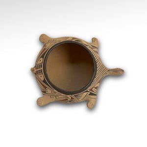 May include: A ceramic pot shaped like a turtle with a brown, black, and red geometric design. The pot is empty and has a wide opening.
