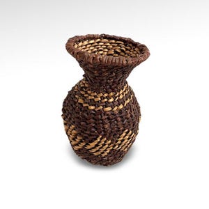 May include: A small, brown and tan woven basket with a rounded base and a flared top.
