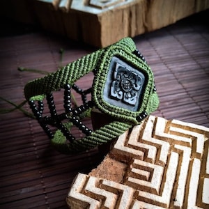 Peut inclure: Un bracelet en macramé vert et noir avec un bouton carré noir orné d'un motif floral.