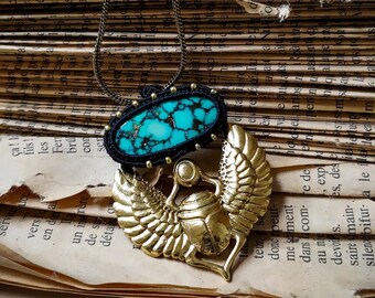 May include: A turquoise gemstone pendant necklace with a gold scarab beetle design. The necklace is on a stack of old books.