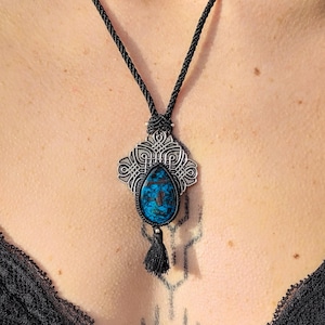 Peut inclure: Un collier en cordon noir avec un pendentif argenté orné d'une pierre précieuse bleue et de détails complexes. Le pendentif est orné d'un pompon.