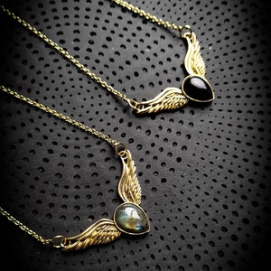 May include: Two gold necklaces with winged pendants. One pendant features a black gemstone, the other a green and gray gemstone.