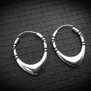 May include: A pair of silver hoop earrings with a unique, slightly pointed oval shape. The earrings have a textured design around the edge.