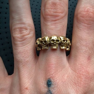 Puede incluir: Un anillo de oro con un diseño de cinco calaveras conectadas.
