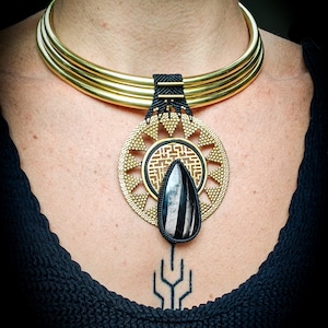 May include: A gold choker necklace with a black and white stone pendant. The pendant is surrounded by a gold circle with a geometric design.