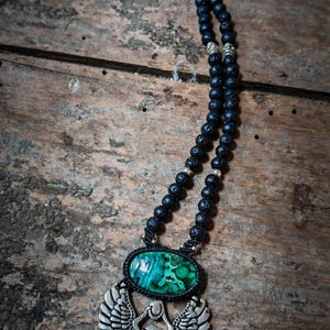 May include: A black lava rock beaded necklace with a silver scarab beetle pendant featuring a green malachite stone.