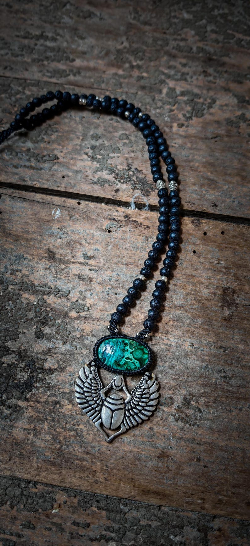 May include: A black lava rock beaded necklace with a silver scarab beetle pendant featuring a green malachite stone.