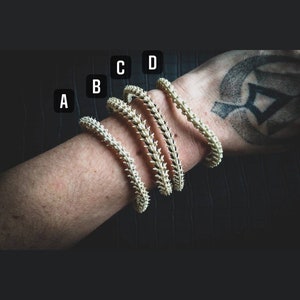 Peut inclure: Quatre bracelets en os blanc avec un motif en pointe. Les bracelets sont empil&eacute;s sur le poignet d'une personne, le plus petit bracelet en bas et le plus grand en haut.