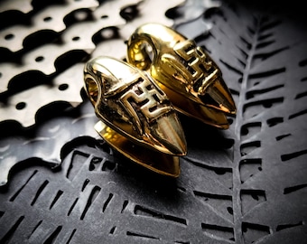 Peut inclure: Une paire d'écarteurs d'oreilles de couleur or avec des motifs complexes. Les écarteurs sont en forme de cœur et ont une pointe pointue.