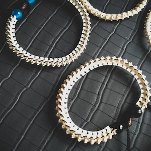 Peut inclure: Trois bracelets en os blanc avec des perles noires et bleues. Les bracelets sont sur une surface textur&eacute;e noire.