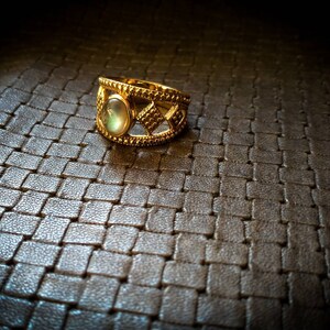 Peut inclure: Une bague en or avec une grande pierre précieuse ronde et irisée sertie dans un motif géométrique.