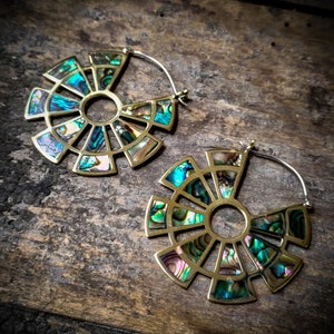 Peut inclure: Une paire de grandes boucles d'oreilles circulaires en laiton avec un motif géométrique. Les boucles d'oreilles sont décorées de morceaux d'ormeau iridescent.