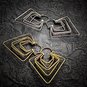 Peut inclure: Deux paires de boucles d'oreilles géométriques. Une paire est argentée, l'autre dorée. Chaque boucle d'oreille présente une série de formes carrées imbriquées, créant un effet superposé. Les boucles d'oreilles sont présentées sur un fond noir texturé.