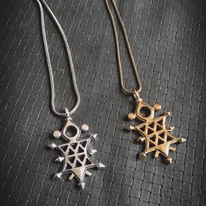 Peut inclure: Deux colliers avec des pendentifs géométriques. L'un a une chaîne et un pendentif argentés, l'autre une chaîne et un pendentif dorés. Les pendentifs sont tous deux complexes et ont un motif en forme d'étoile.