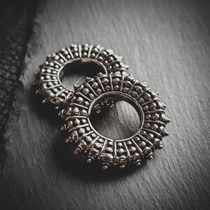 May include: Two silver-toned metal ear gauges with a circular design and a textured surface. The gauges are stacked on top of each other.
