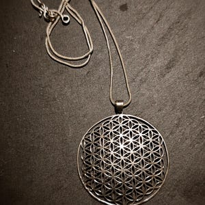 Peut inclure: Un collier en argent avec un grand pendentif rond orné d'un motif géométrique détaillé. Le pendentif est un motif de fleur de vie.