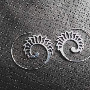 Peut inclure: Une paire de boucles d'oreilles créoles en argent avec un motif en spirale. Les boucles d'oreilles sont en métal et ont un design délicat et complexe.