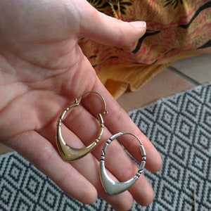 May include: A pair of hoop earrings, one gold and one silver, with a crescent moon shape. The earrings are held in a hand.