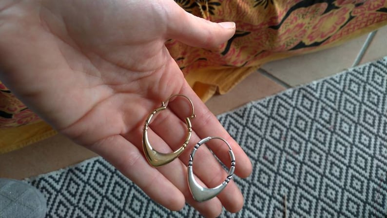 May include: A pair of hoop earrings, one gold and one silver, with a crescent moon shape. The earrings are held in a hand.