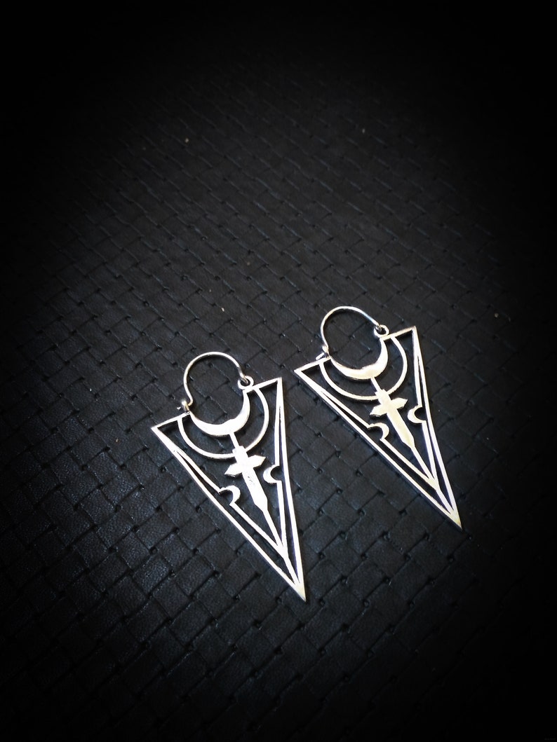 May include: A pair of silver triangle shaped earrings with intricate geometric designs. The earrings have a hoop at the top and dangle from the ear.